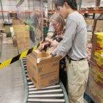 Volunteers packing a box on a conveyor belt