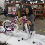 A volunteer putting a handle bar on a purple/pink bike