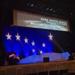 A theatre stage with stary night sky with a tree, chair and a big gray rock