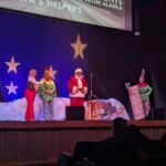 Santa, 2 elves, and someone else standing on the theatre stage