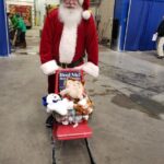 Santa with a chair on top of skis that has a basket filled with stuffed animals