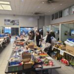volunteers carring bags filled with toys surrounded by tables filled with items